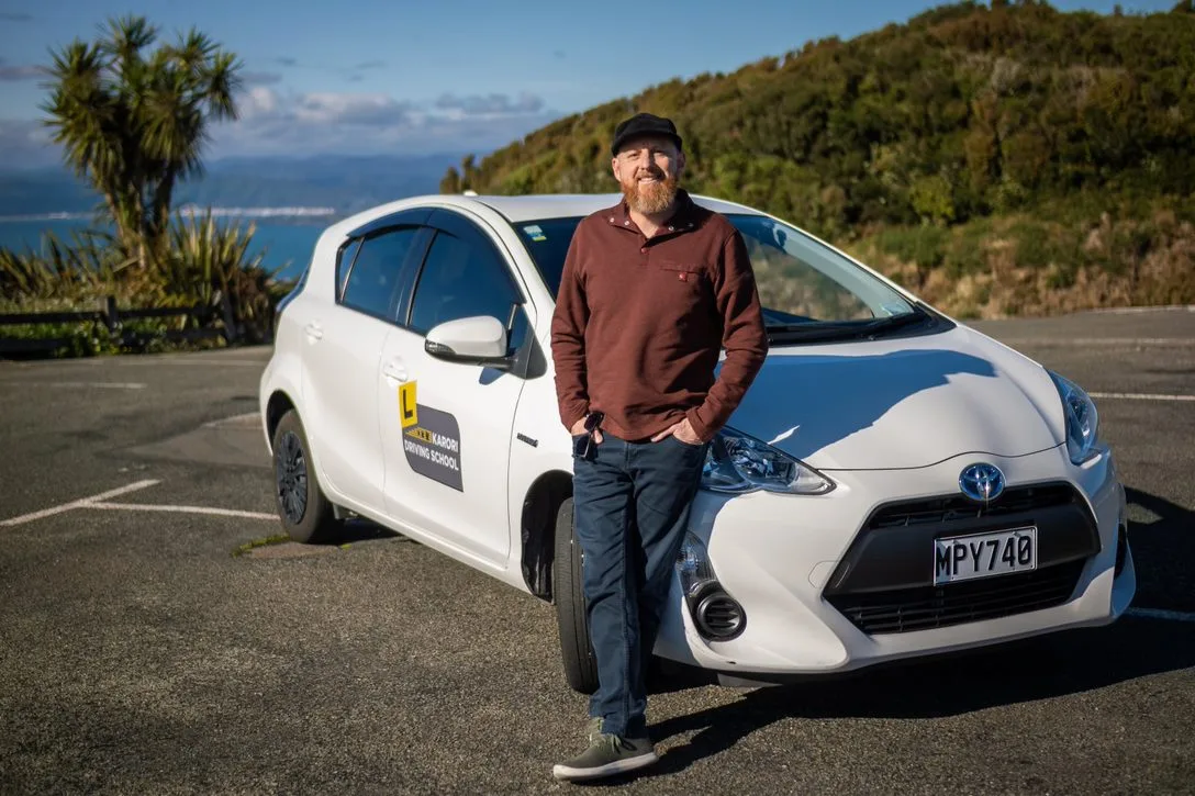 Marcel, your driving instructor, standing beside the Karori Driving School vehicle.